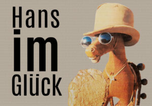Schrift: Hans im Glück, daneben ein Tier, wahrscheinlich Hans mit Goldklumpen, Sonnenbrille und Hut